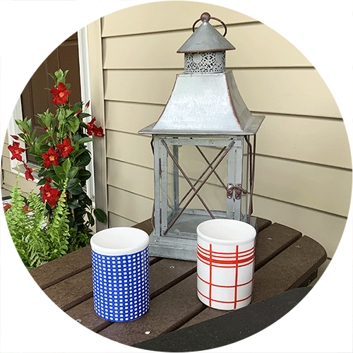 A metal lantern with two cups in front, one with blue plaid and one with red plaid.